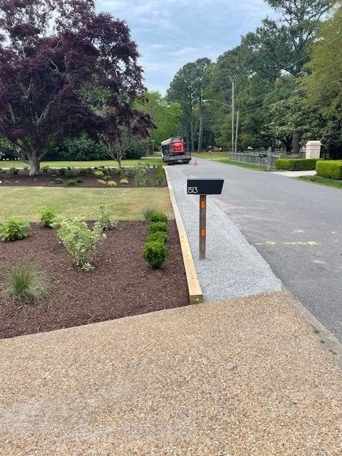 Gravel driveway leading to a mailbox, small shrubs, and a red machine in the distance.