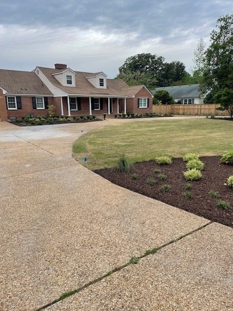 Brick house with manicured lawn, curved driveway, and newly mulched flowerbeds.