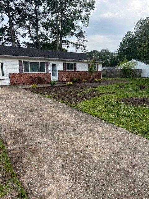 A house with a red brick facade and a concrete driveway. Landscaped yard with freshly turned earth.