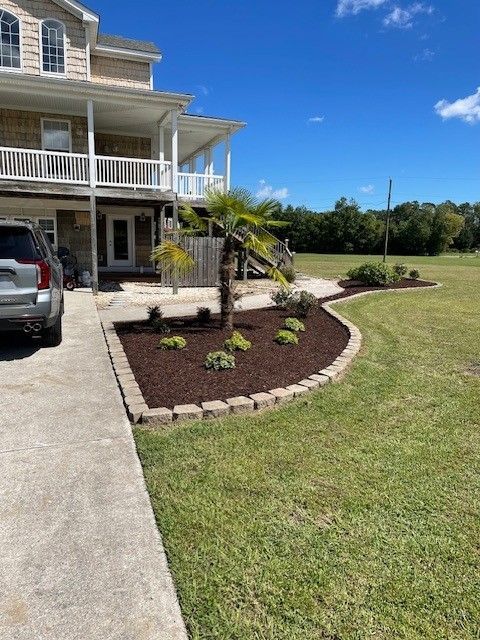 Two-story beige house with a landscaped yard and a car parked in the driveway on a sunny day.