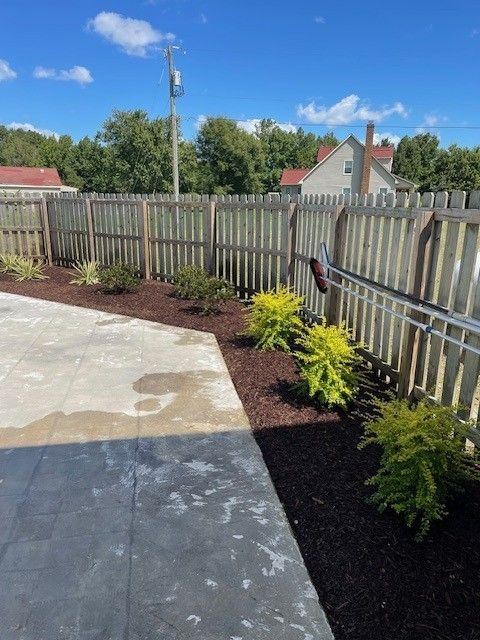A backyard with a fence, plants, and a patio. Sunny day.