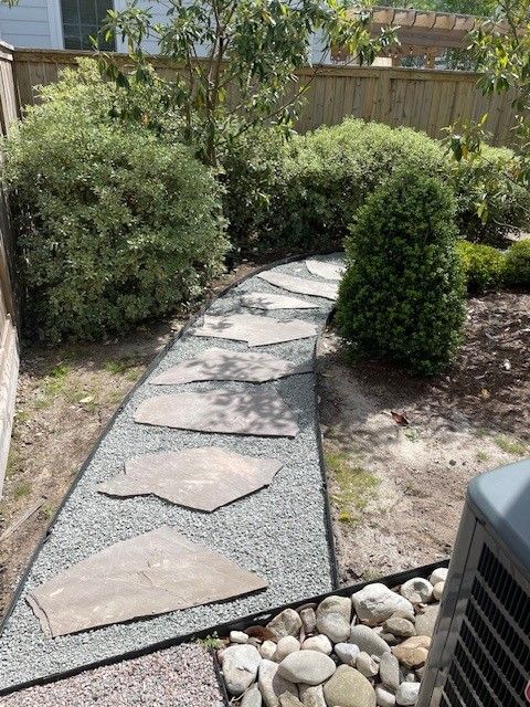Stone pathway through a backyard garden, bordered by pebbles and greenery.