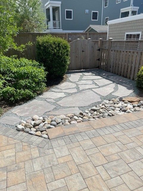 Stone patio with flagstone path, rock border, and wooden fence in a yard.