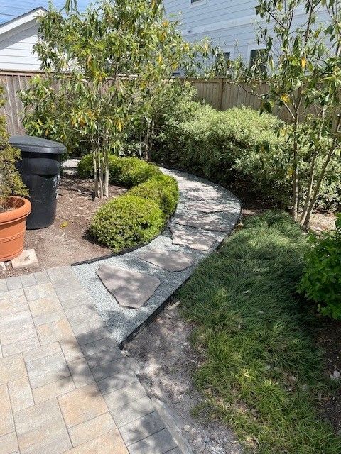 Stone pathway curves through a backyard garden with hedges, trees, and grass.
