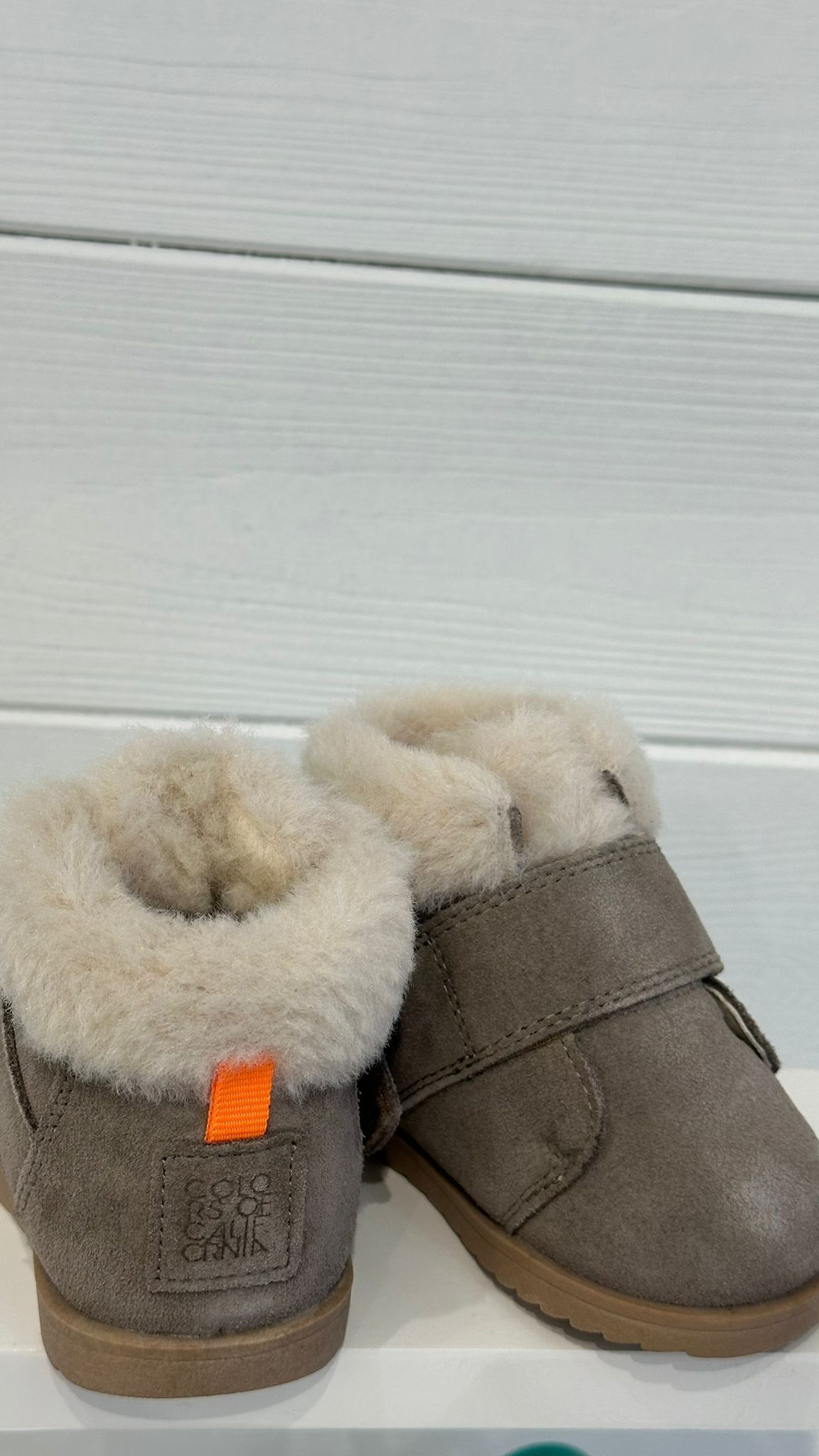 Due stivali per bambini in pelle scamosciata grigia con fodera in pelliccia sintetica color cuoio su uno scaffale bianco.