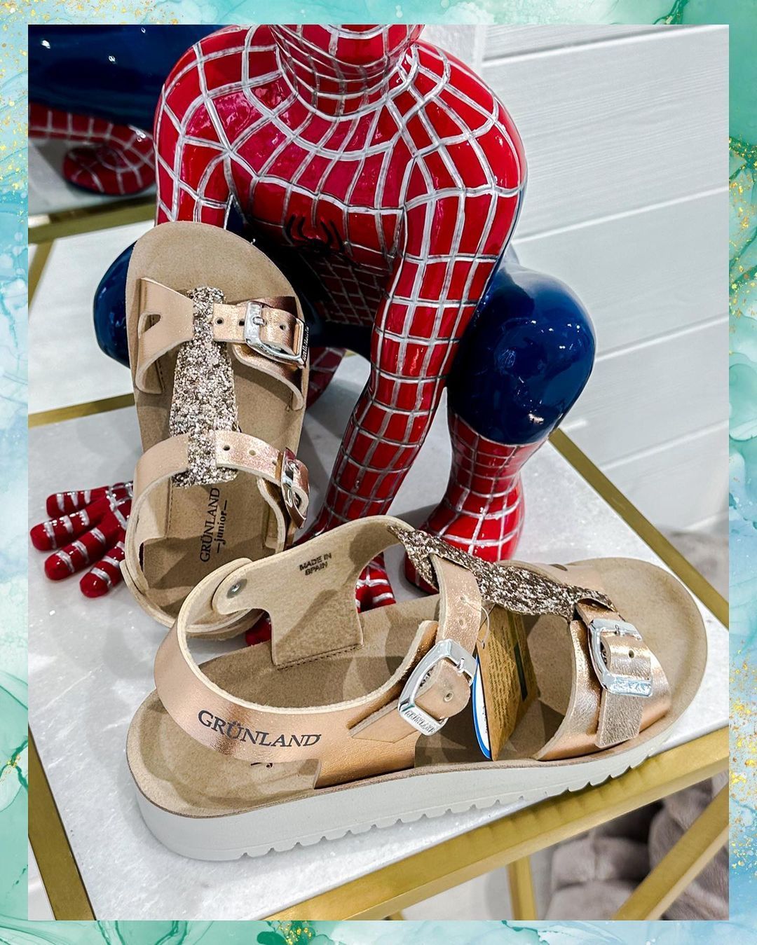 Sandali color oro rosa con dettagli glitterati davanti alla statua di Spider-Man.