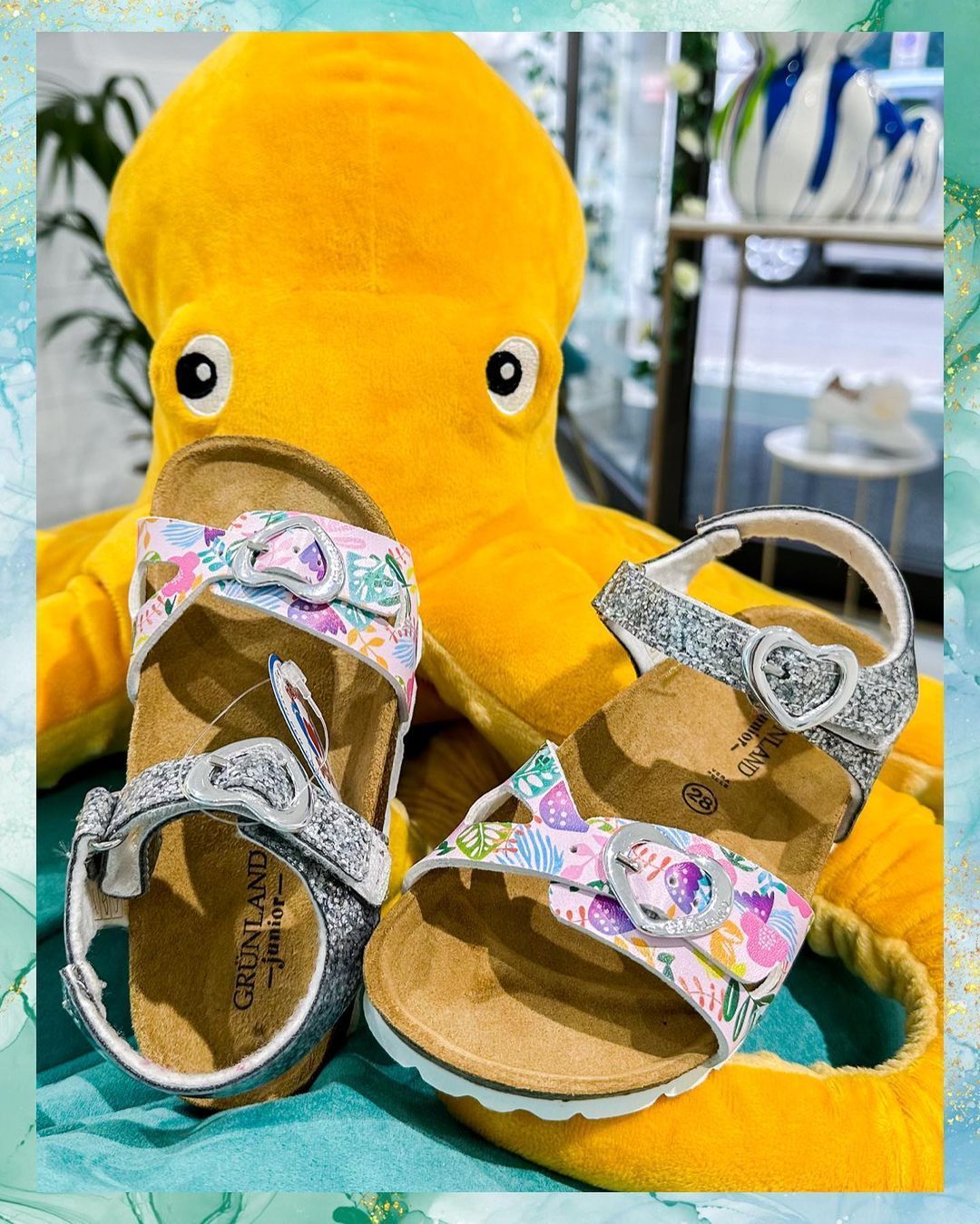 Due paia di sandali per bambini con disegni floreali accanto a un grande peluche a forma di polpo giallo.