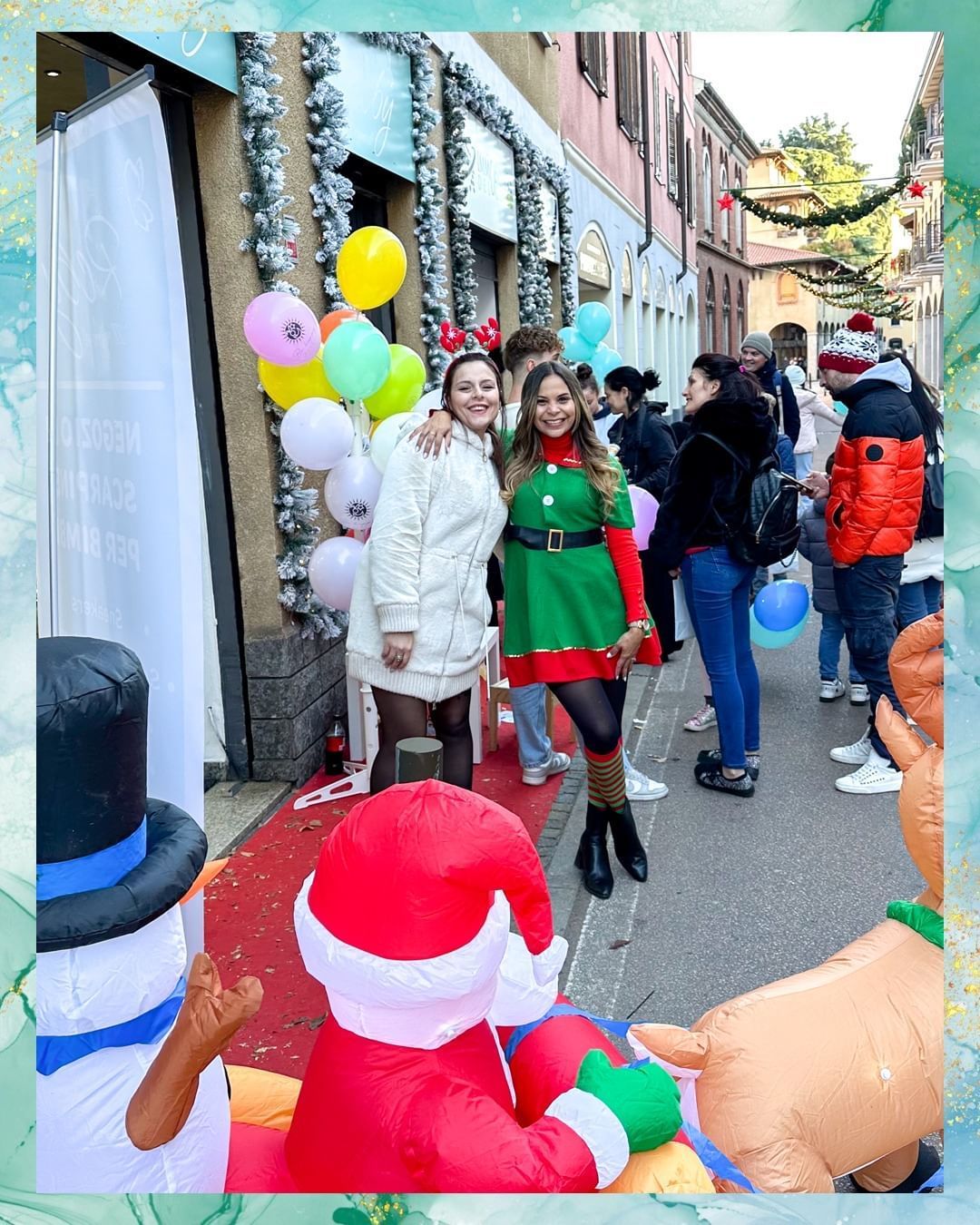 Due donne posano con palloncini e un pupazzo di neve gonfiabile davanti a un negozio; decorazioni natalizie.