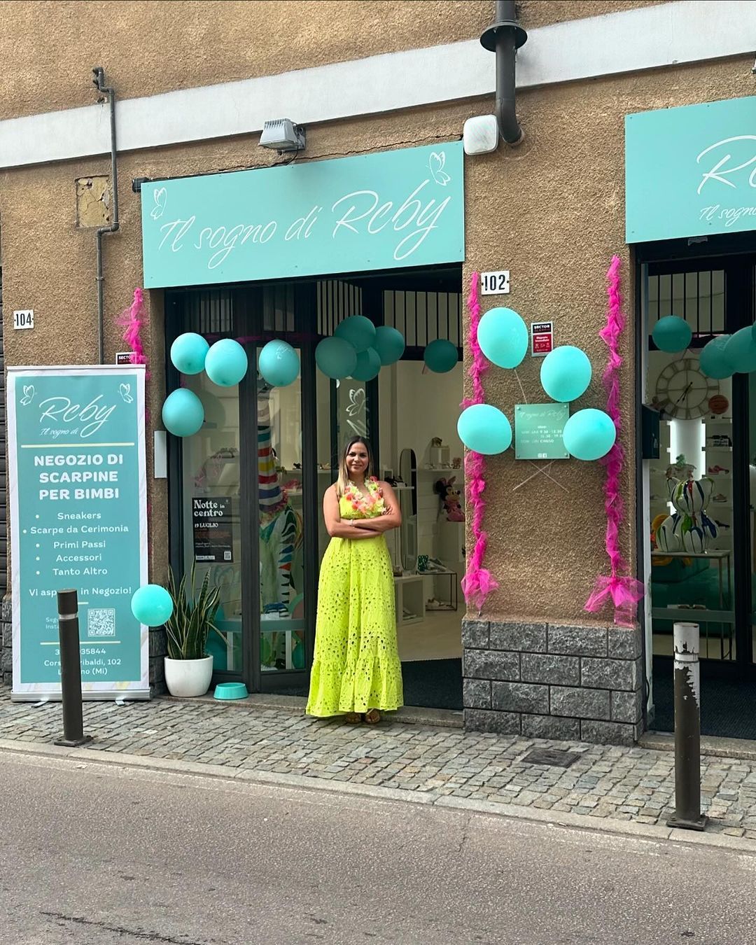 Una donna con un abito color lime sta fuori da un negozio con palloncini e insegne turchesi.