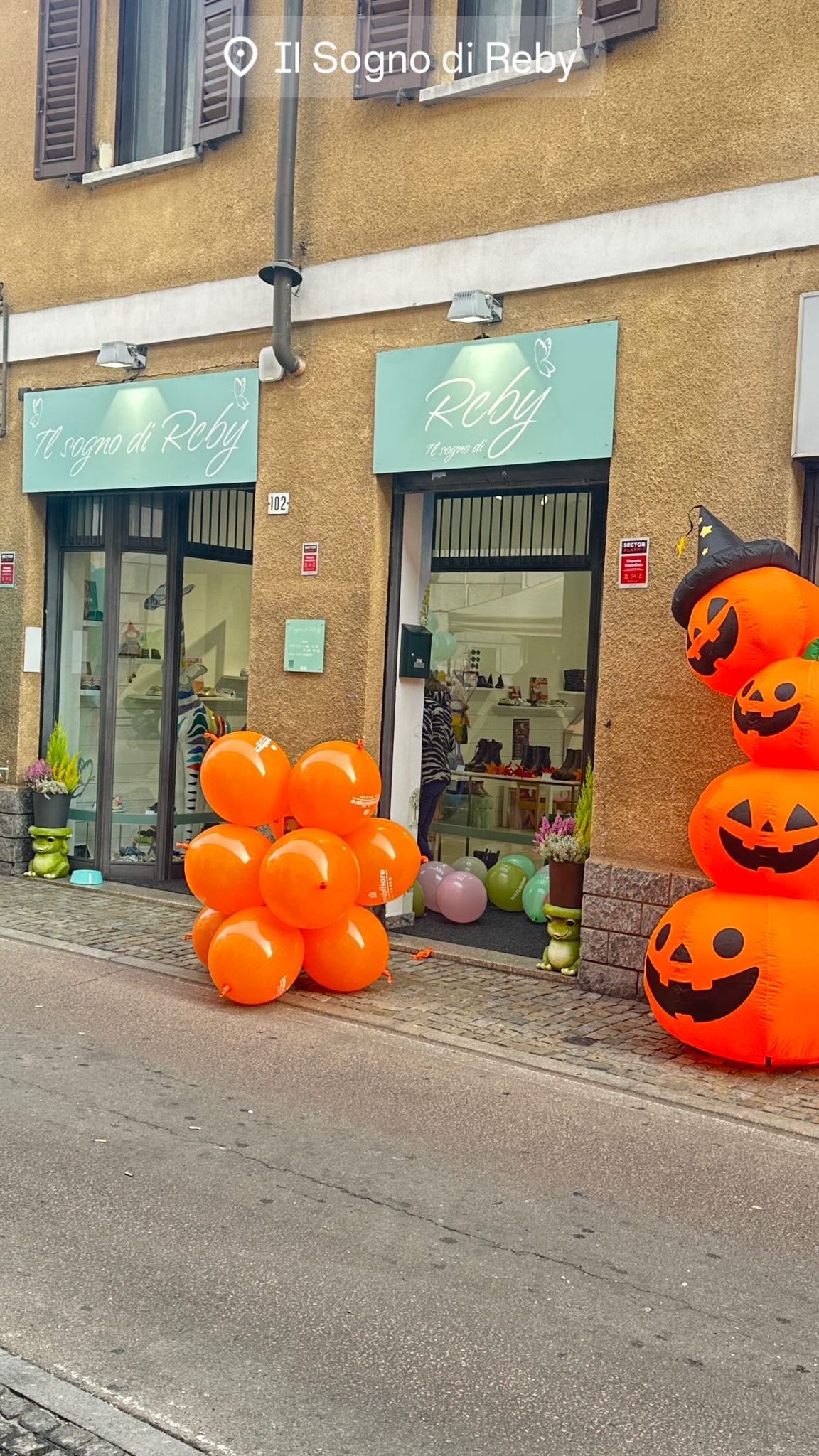 Vetrina con insegna color verde acqua, palloncini arancioni e una decorazione a forma di zucca per Halloween.