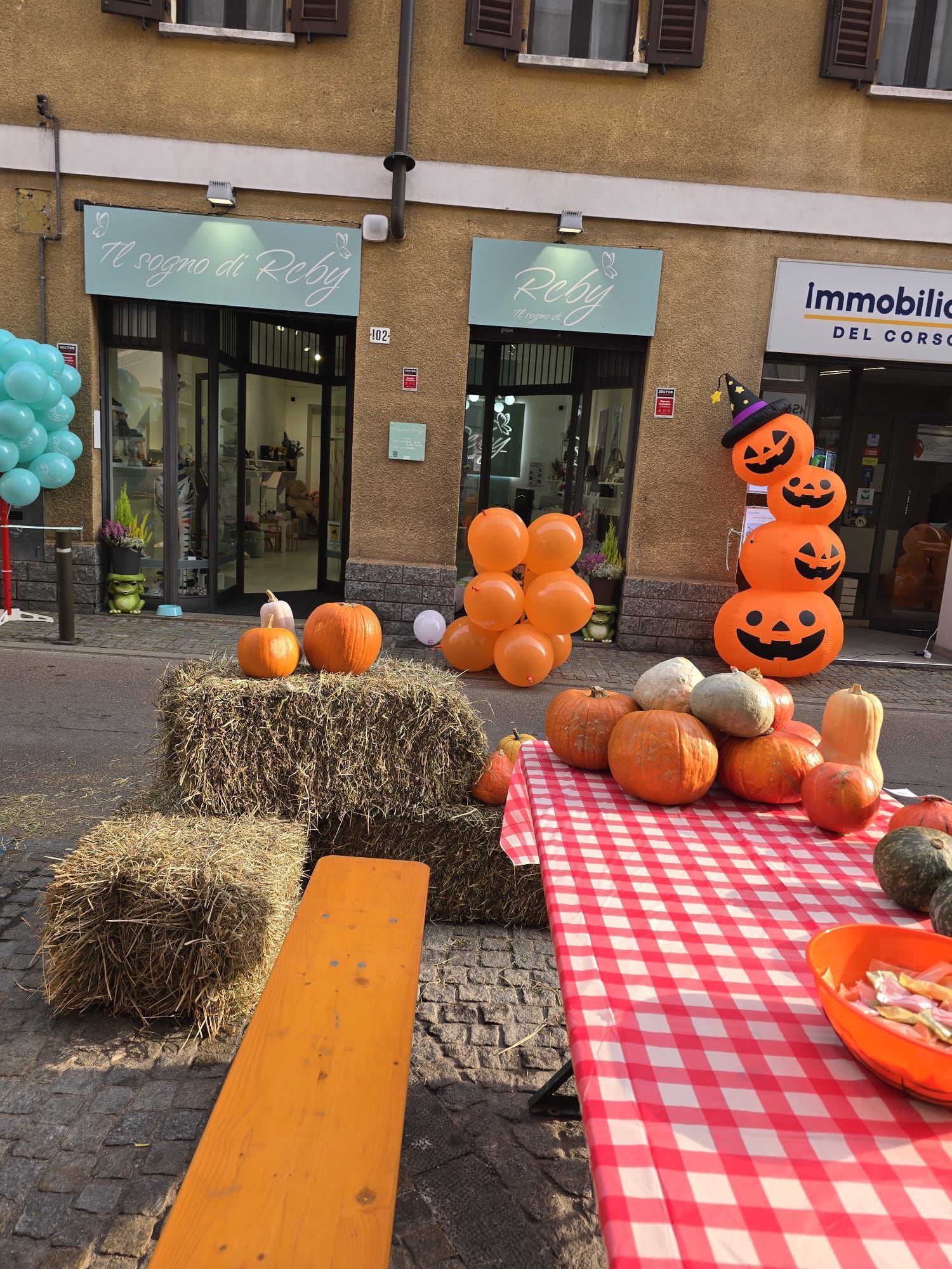 Decorazioni di Halloween davanti ai negozi: zucche, palloncini arancioni, balle di fieno e una pila di zucche.