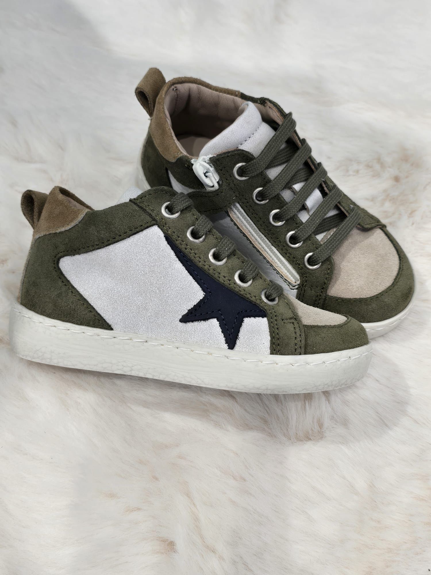 Un paio di sneakers verde oliva e bianche con dettaglio a stella su una superficie di colore chiaro.