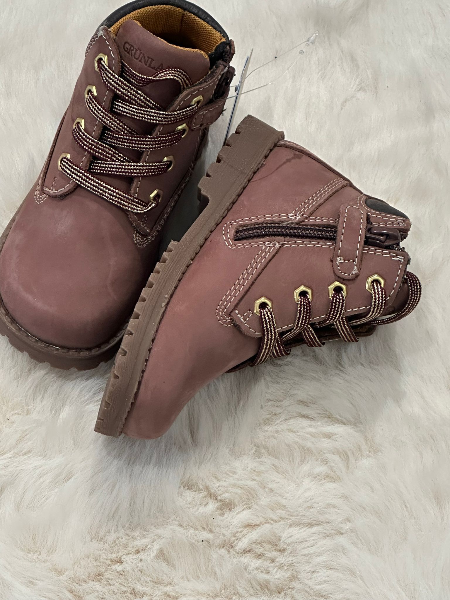 Stivaletti marroni e bordeaux per bambini piccoli, con lacci e cerniere, su un tappeto color crema.