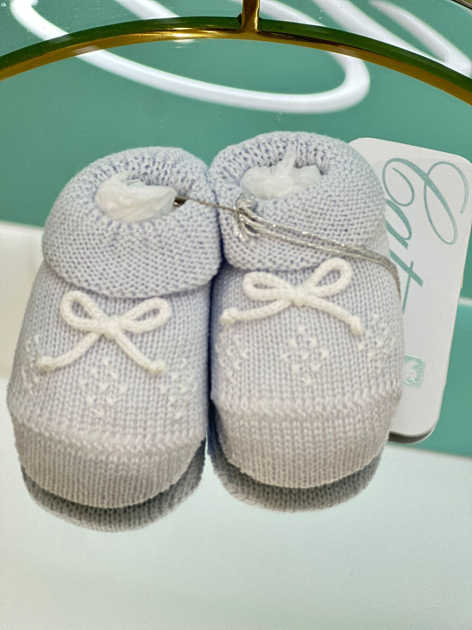 Scarpine blu per neonati con fiocchi bianchi, su una superficie riflettente.