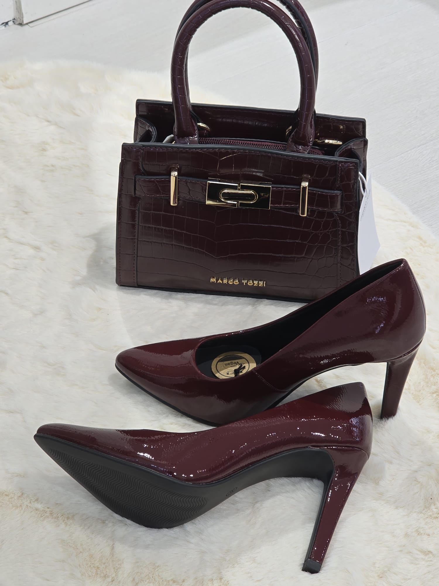 Borsa bordeaux e tacchi alti coordinati su una superficie bianca.