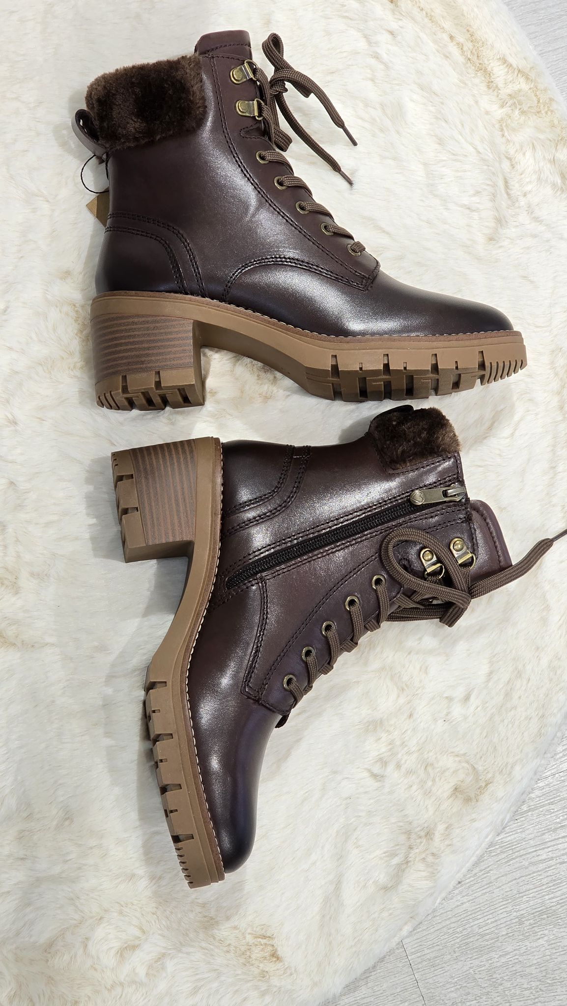 Un paio di stivali stringati in pelle marrone con fodera in pelliccia e tacco spesso su una superficie neutra.