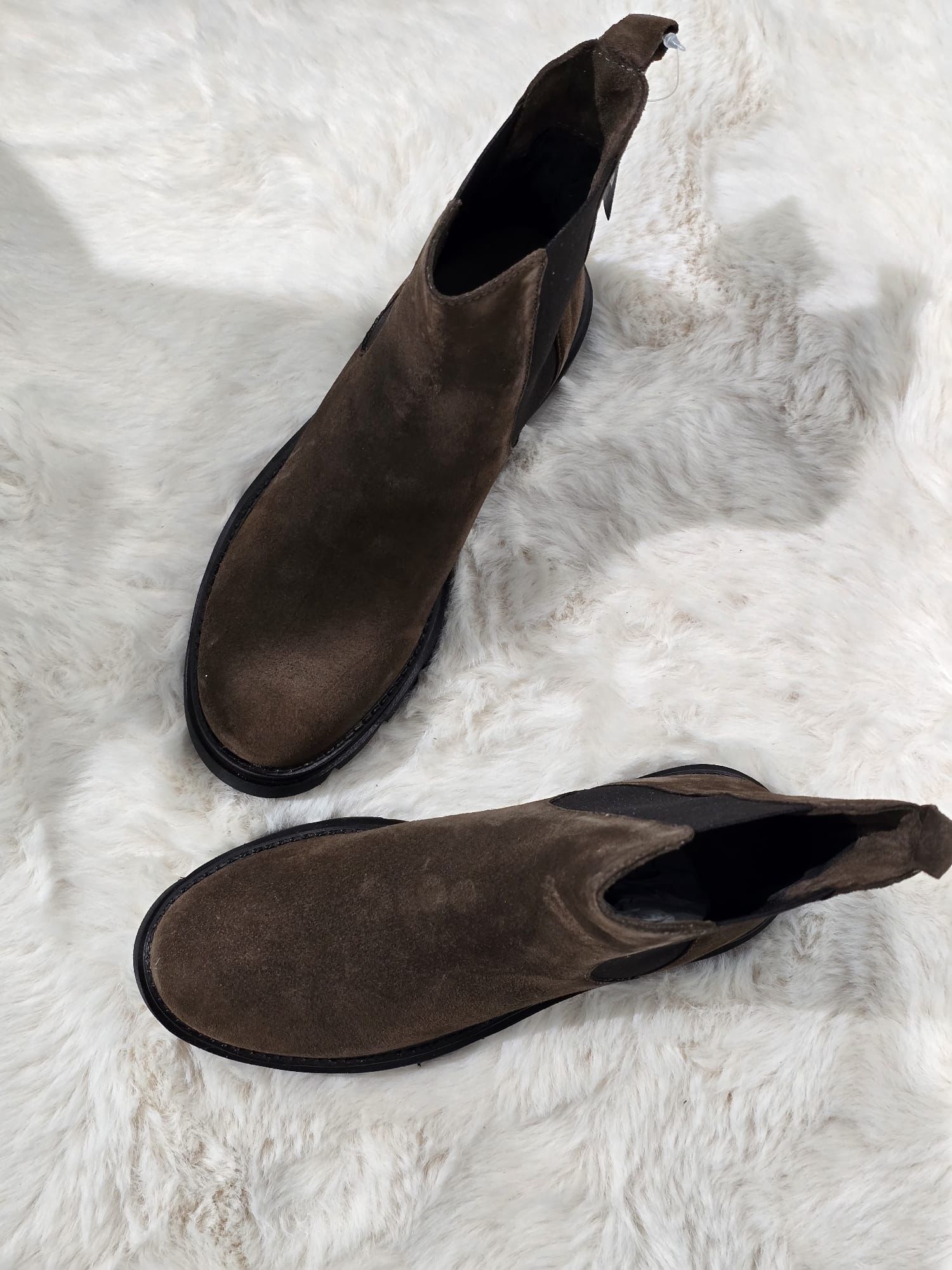 Stivaletti Chelsea in pelle scamosciata marrone su una superficie bianca e soffice.