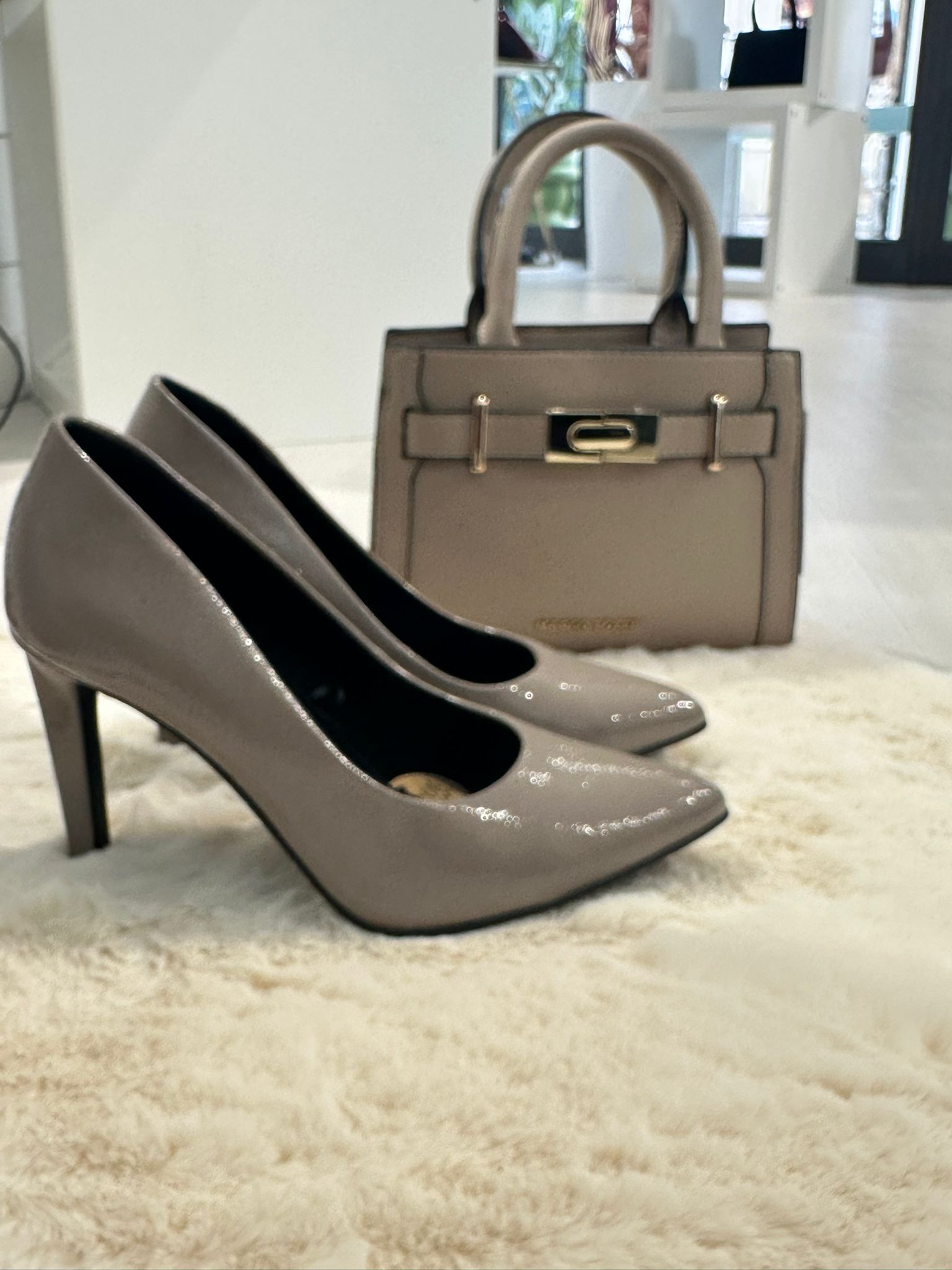 Scarpe con tacco alto color talpa e borsa coordinata su un soffice tappeto.