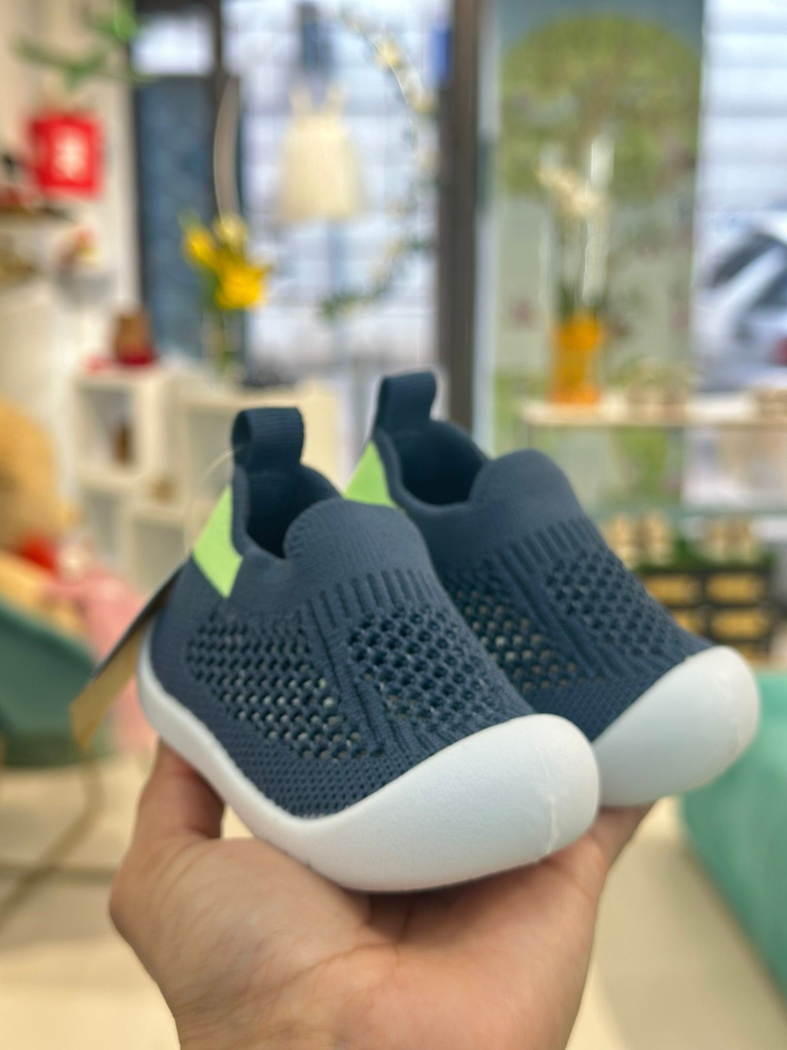 Persona che tiene in mano un paio di scarpine da neonato blu e bianche con un tocco verde; interno di un negozio.