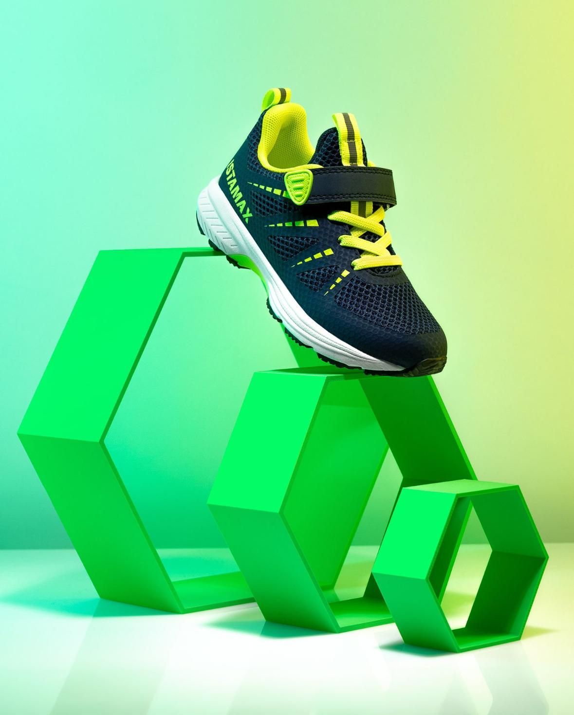 Scarpa sportiva blu navy e verde su tre forme geometriche verdi su uno sfondo sfumato.