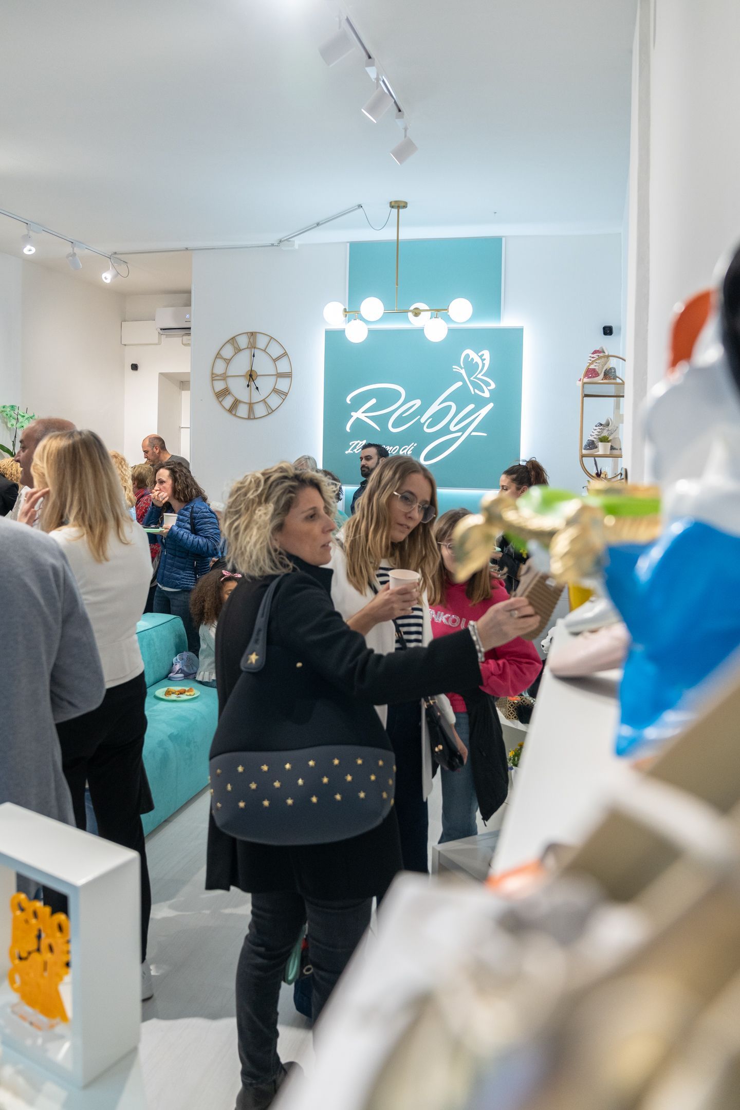 Persone in un negozio luminoso con decorazioni color pastello, una donna esamina un articolo sul bancone.