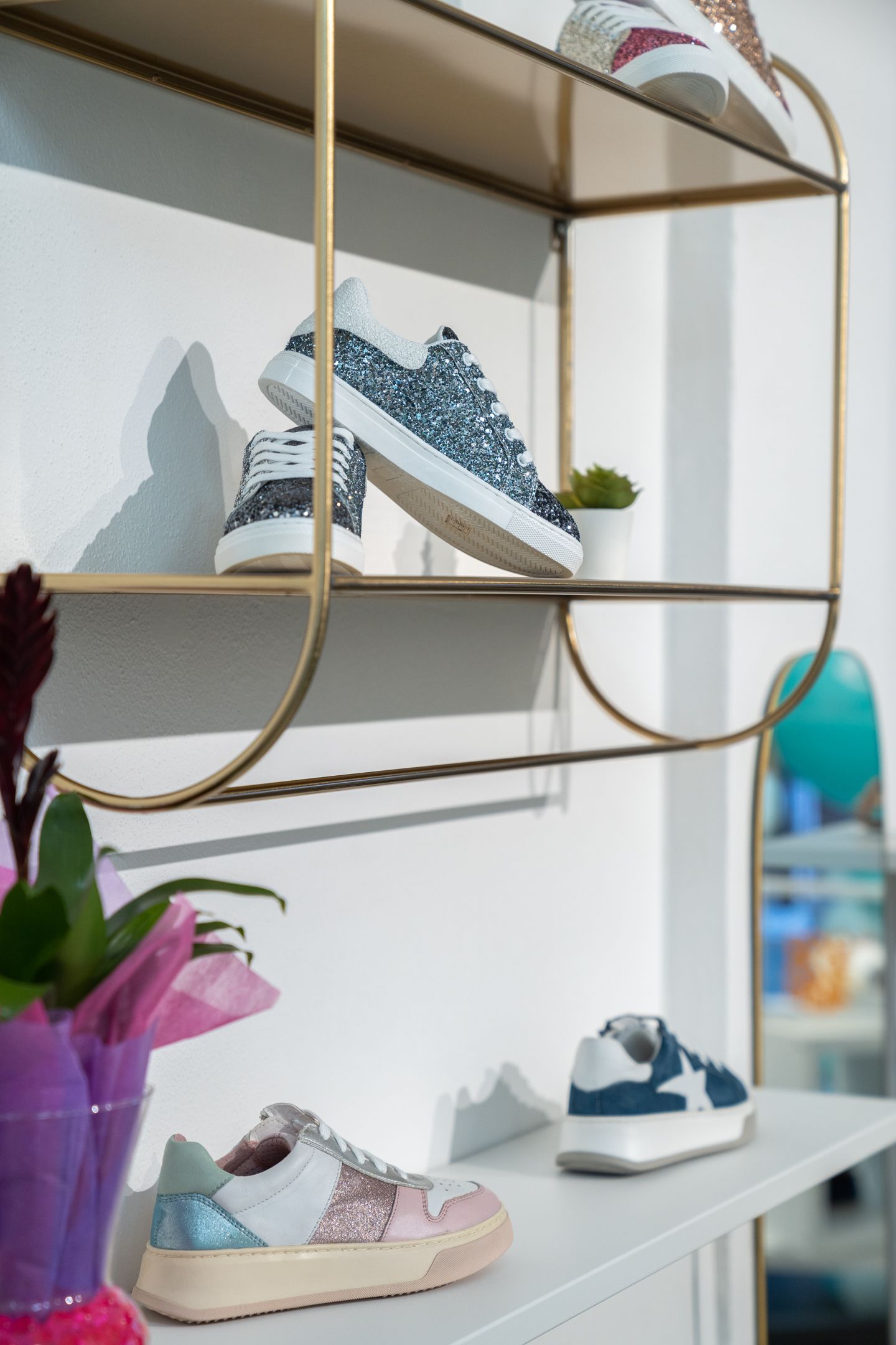 Scarpe esposte su scaffali dorati contro una parete bianca.