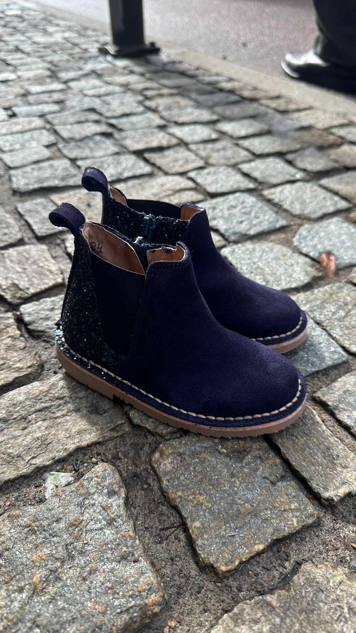 Stivaletti per bambini in pelle scamosciata blu scuro con dettagli scintillanti, su una strada acciottolata.