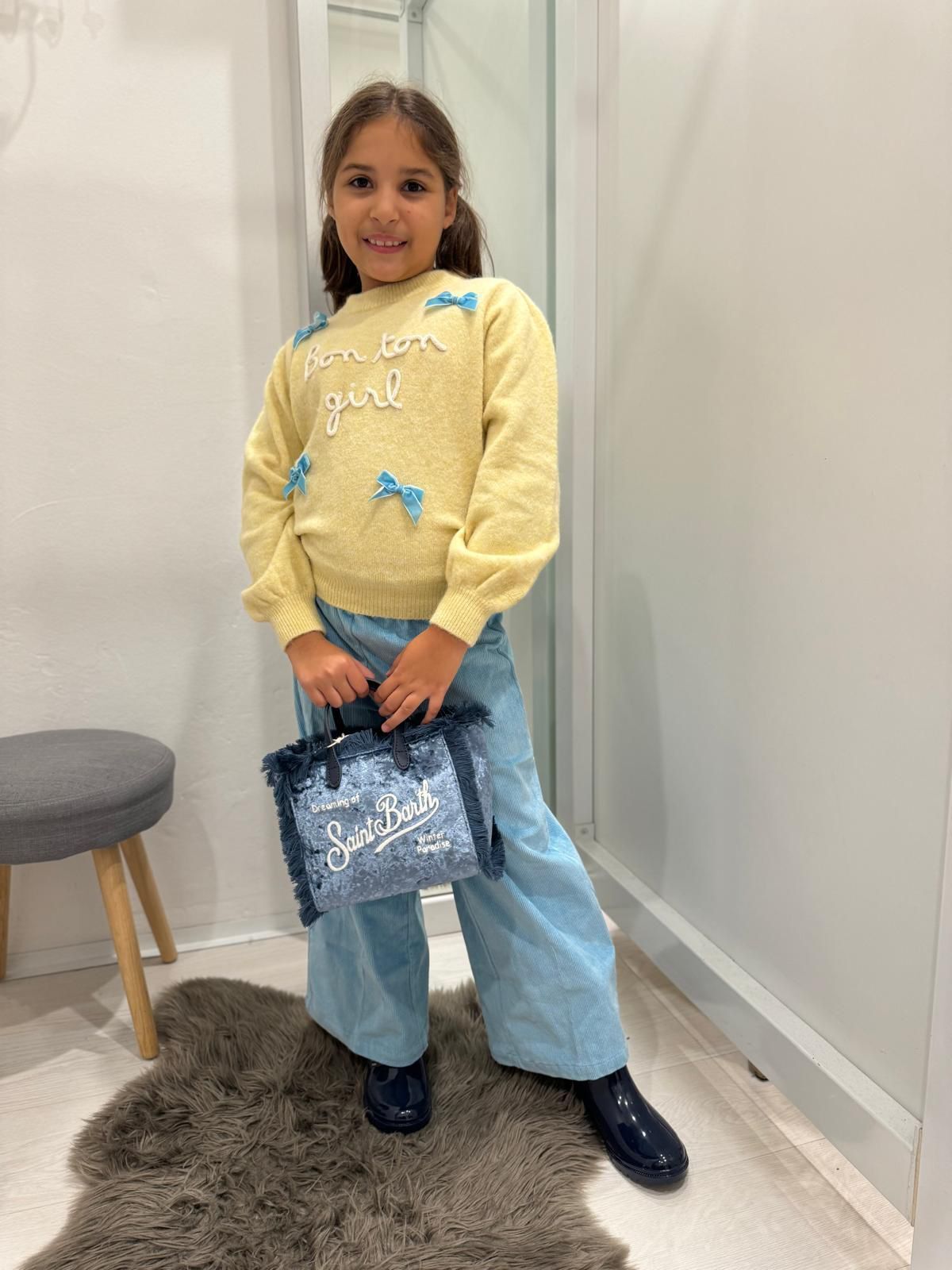 Una ragazza con un maglione giallo e jeans blu tiene in mano una borsa in un negozio al dettaglio.