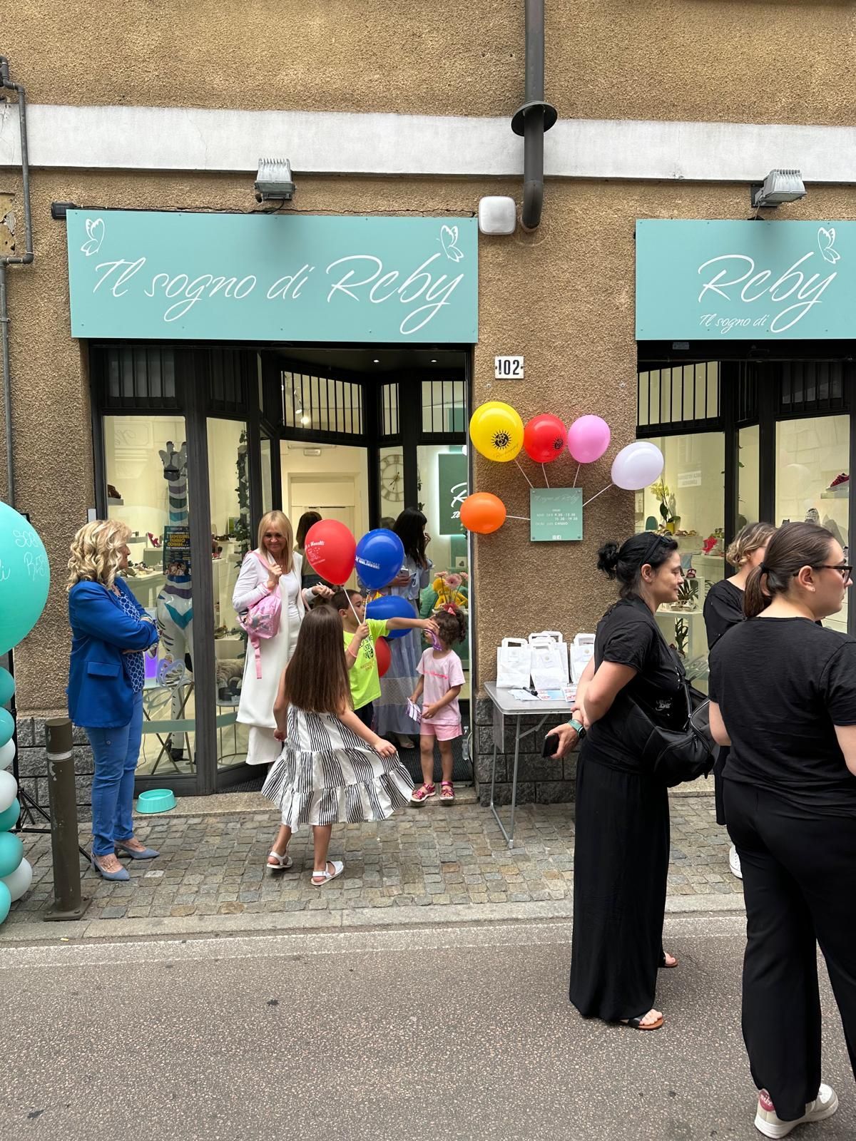 Persone fuori da un negozio con palloncini. L'insegna del negozio recita