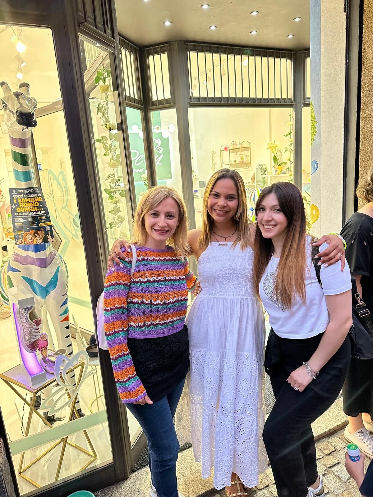 Tre persone sorridenti, in posa davanti alla vetrina di un negozio con all'interno una statua di giraffa.