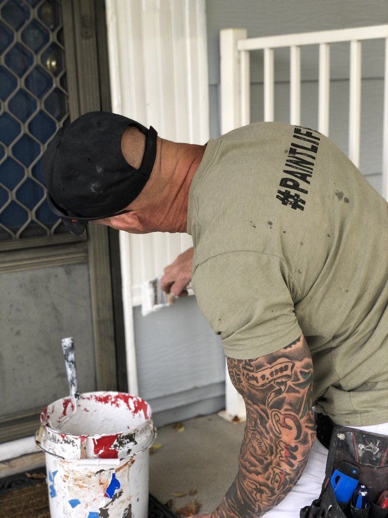 The Idaho Painter is painting a door with a brush and a bucket of paint.