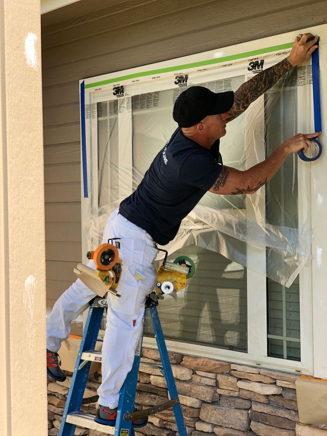 Exterior painting contractor masking a residential window before surface preparation and paint application.