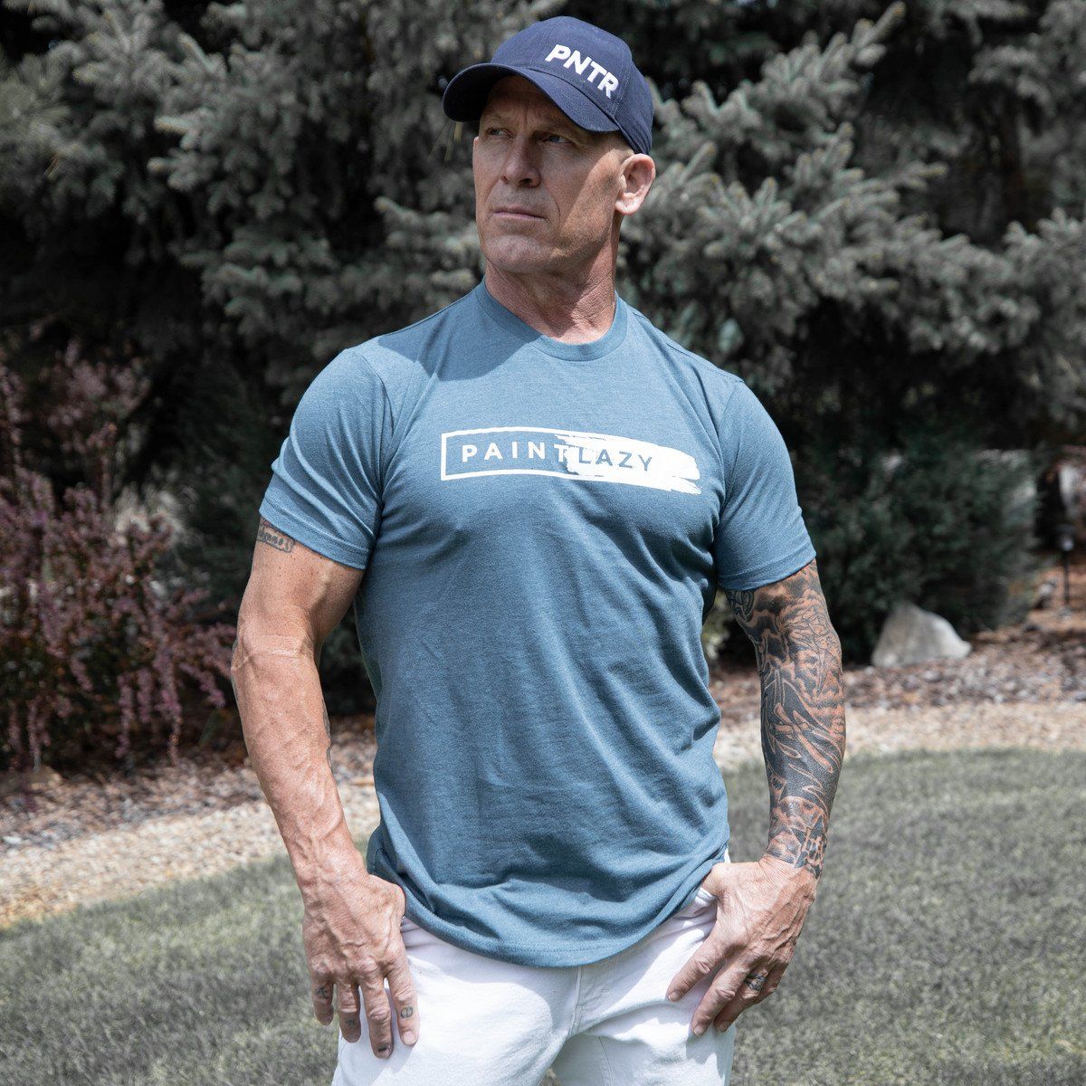 The Idaho Painter wearing a blue t-shirt and a hat is standing in the grass.