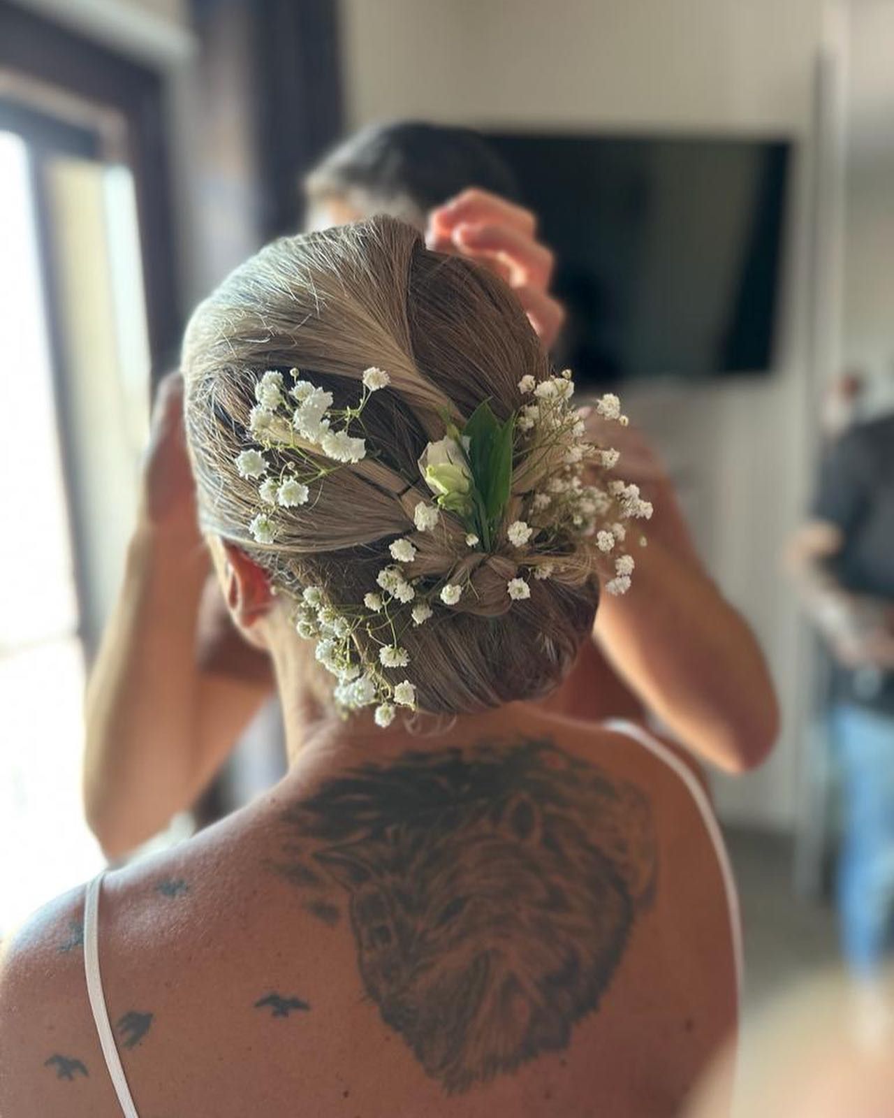 Una donna con un tatuaggio sulla schiena indossa dei fiori tra i capelli.