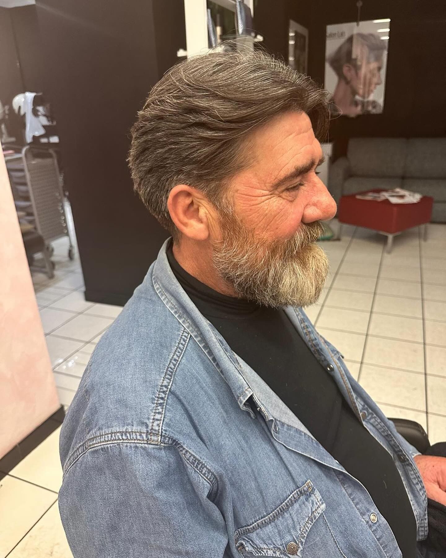 Un uomo con la barba e una giacca di jeans è seduto in un salone.