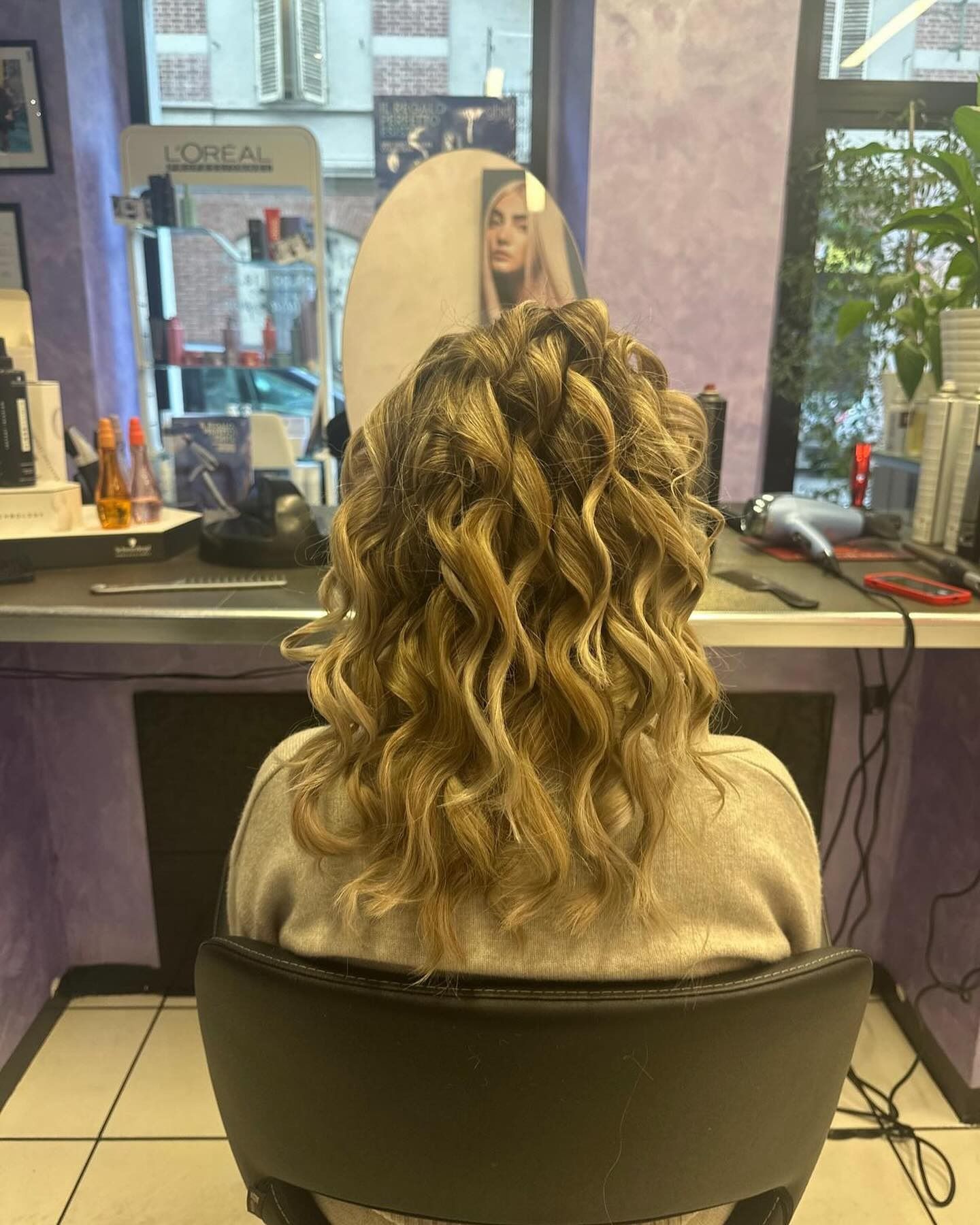 Una donna è seduta su una sedia davanti allo specchio in un salone da parrucchiere.