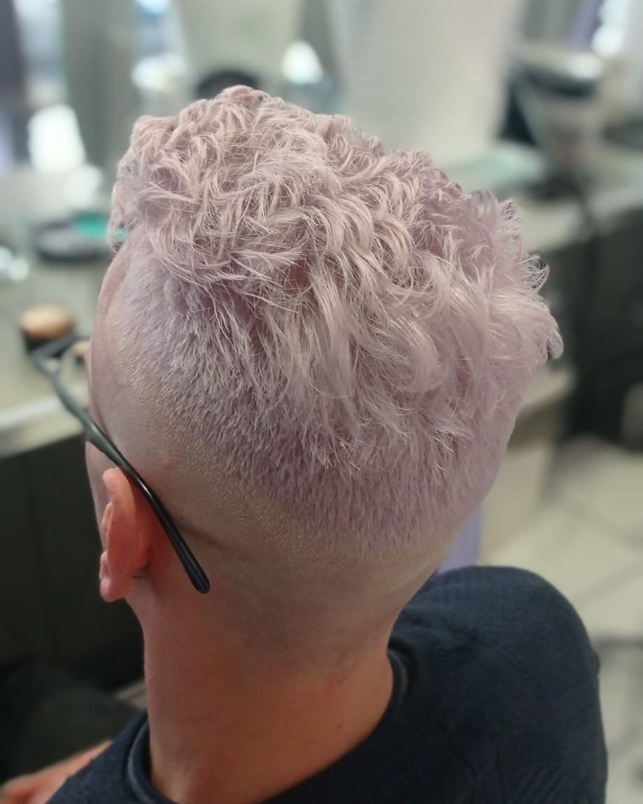 Un uomo con i capelli rosa e gli occhiali è seduto su una sedia.