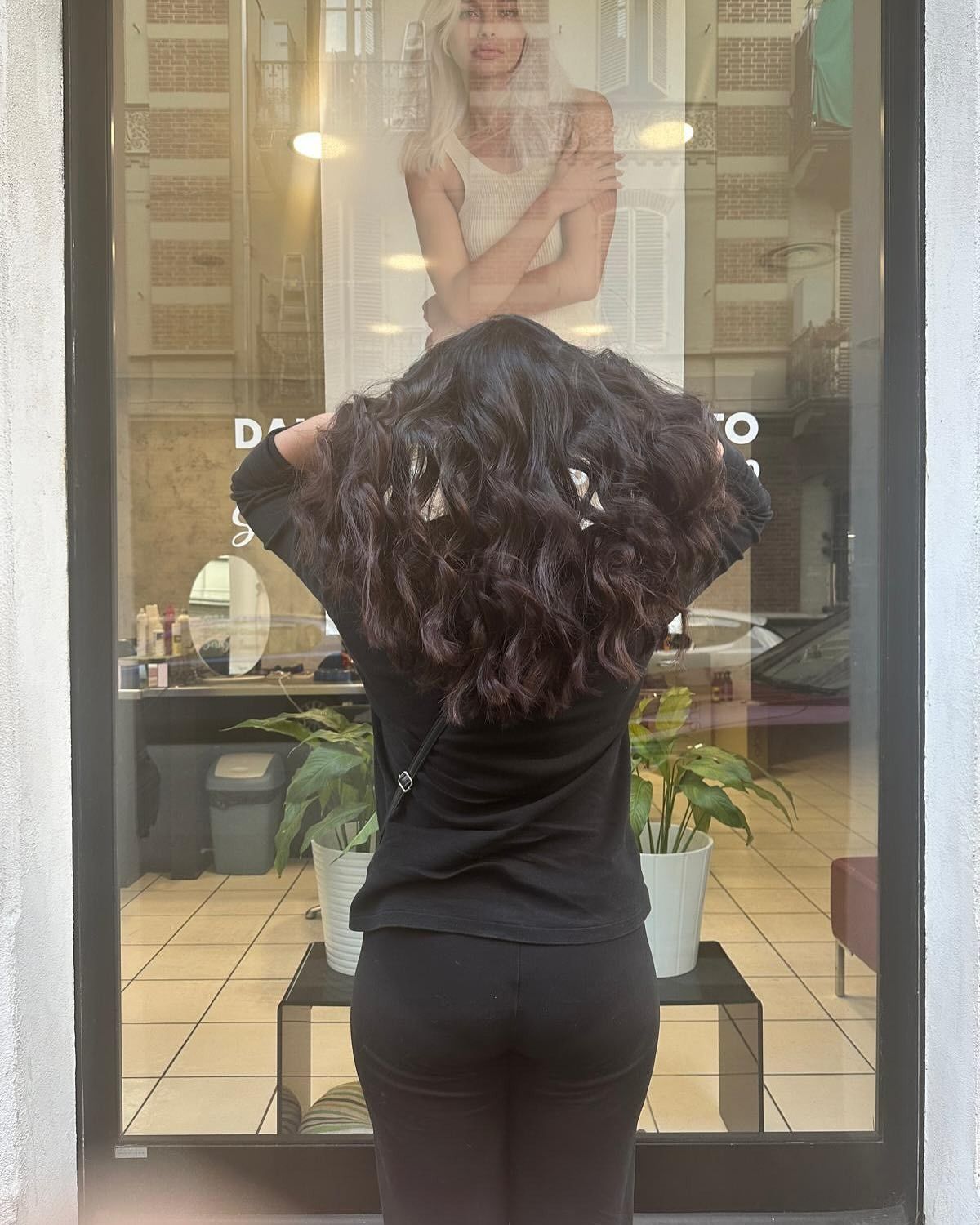 Una donna è in piedi davanti a una finestra e si guarda i capelli.