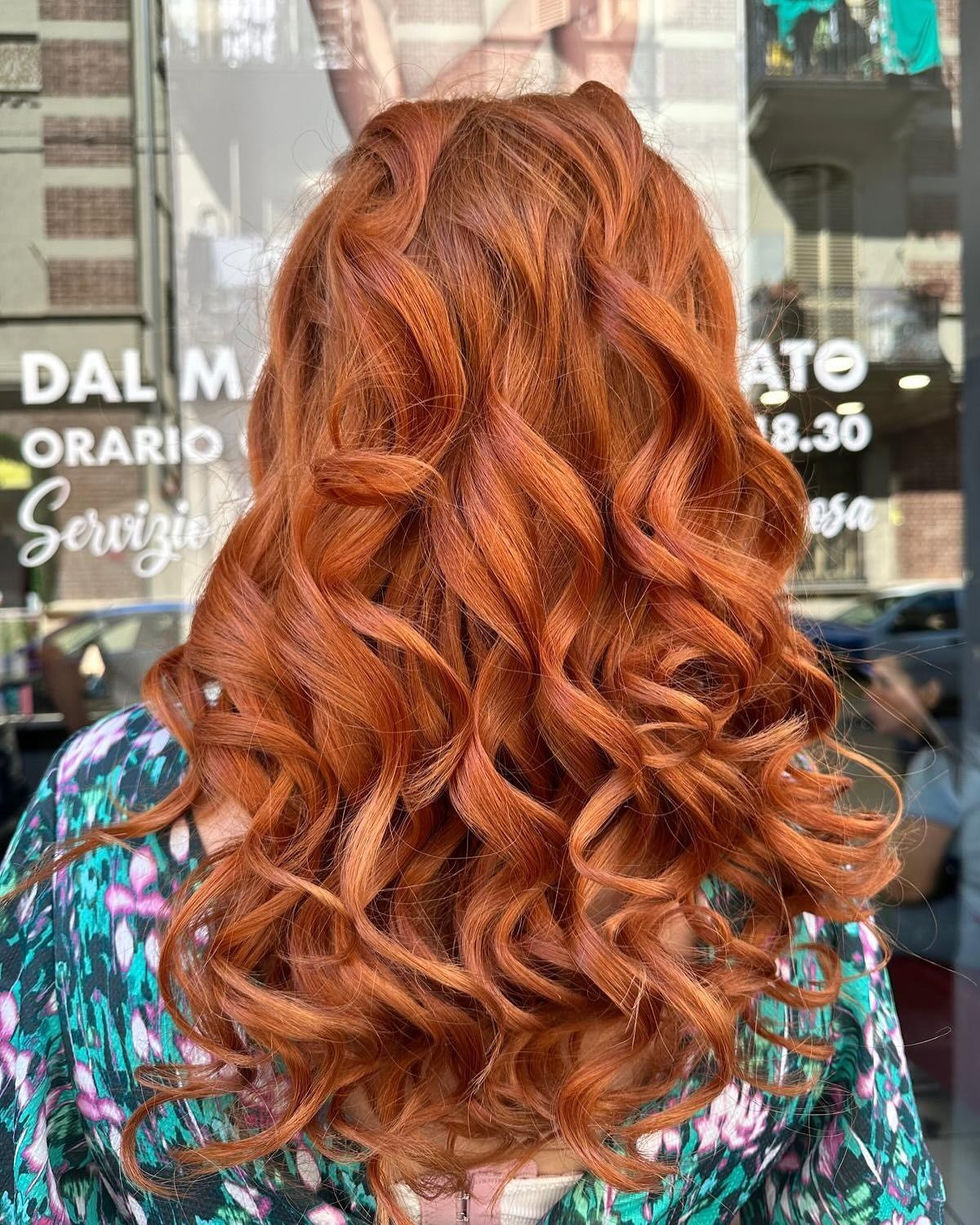 Una donna con i capelli rossi e ricci è in piedi davanti a un edificio.