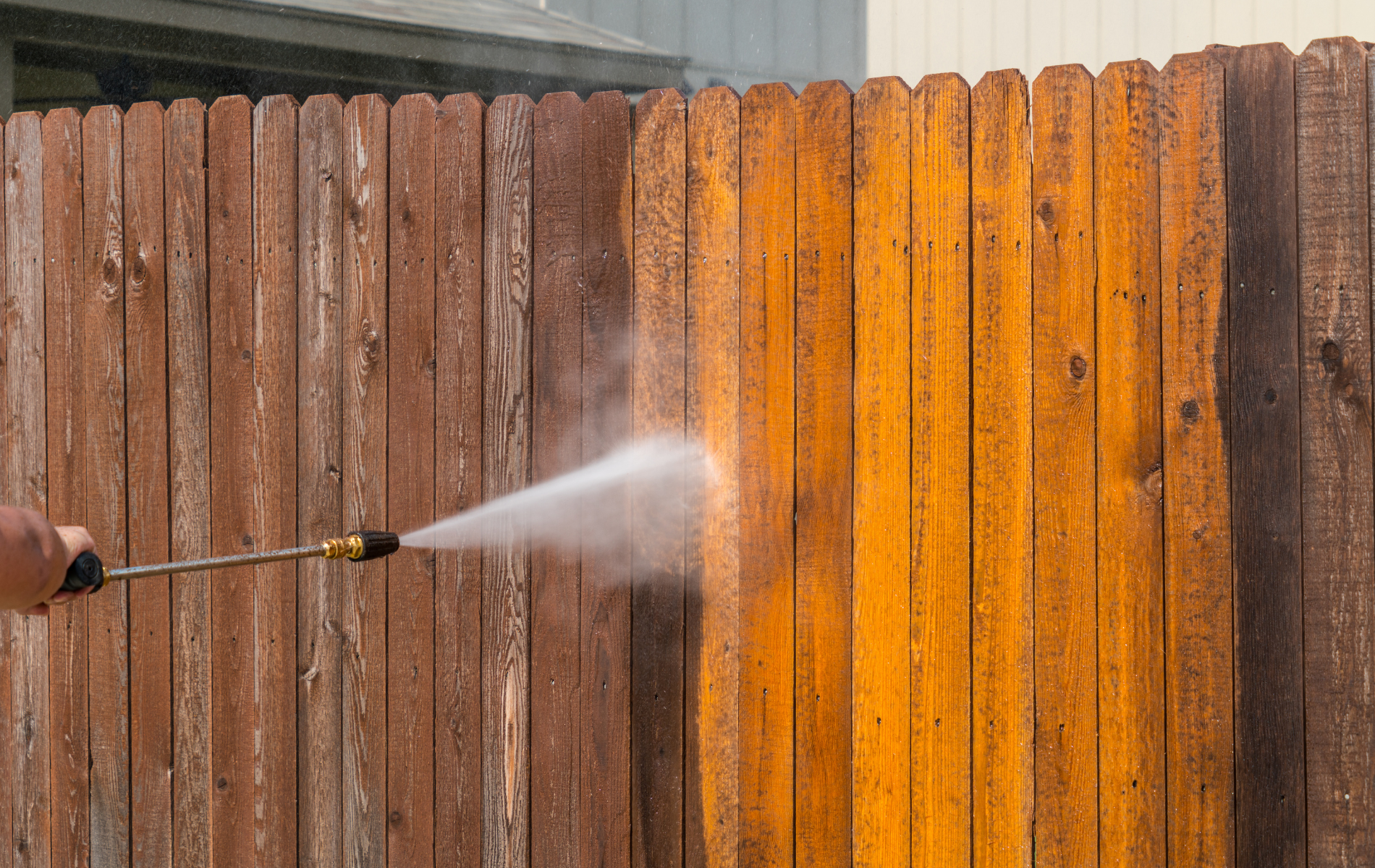 A person is using a high pressure washer to clean a wooden fence.