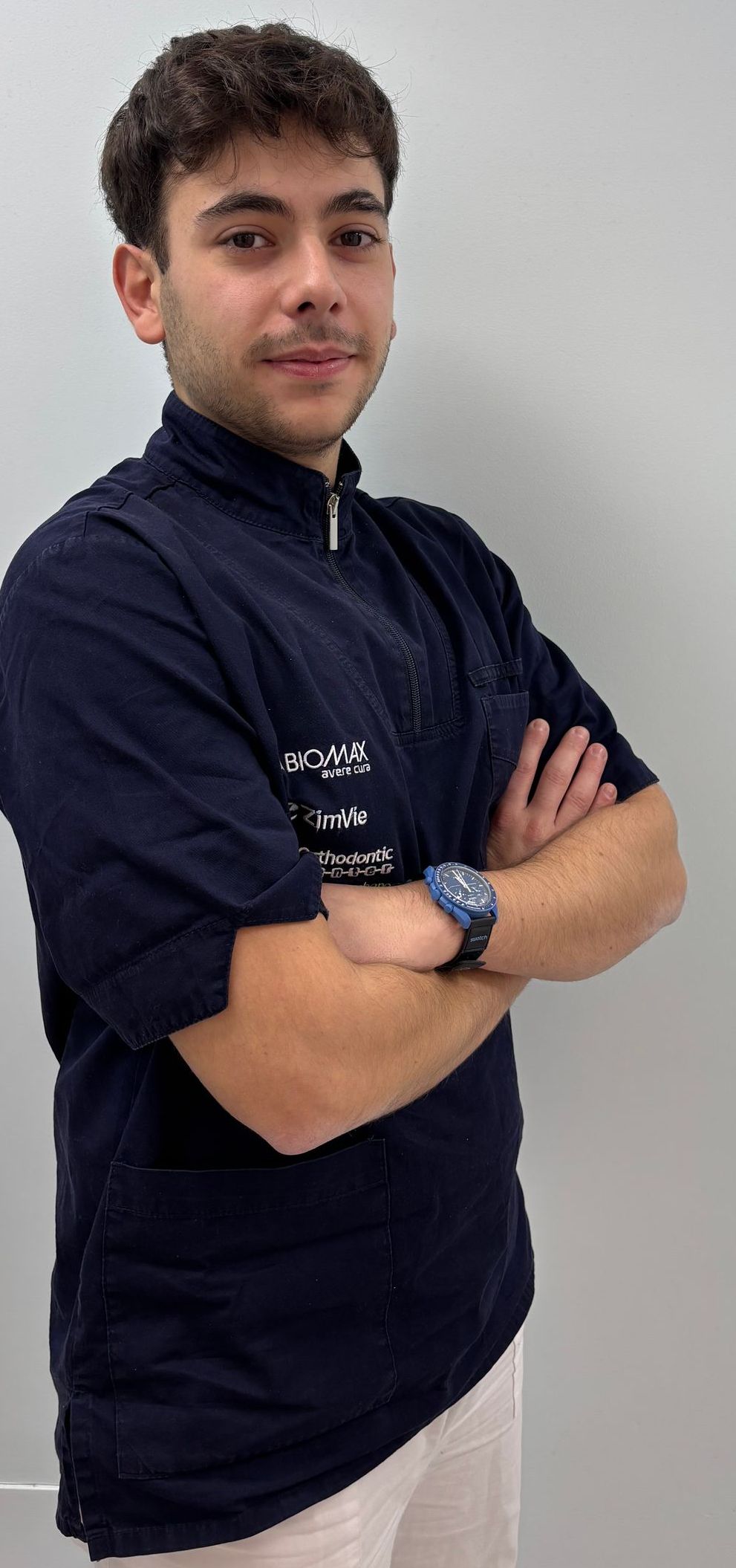 Un giovane con una camicia blu è in piedi con le braccia incrociate.