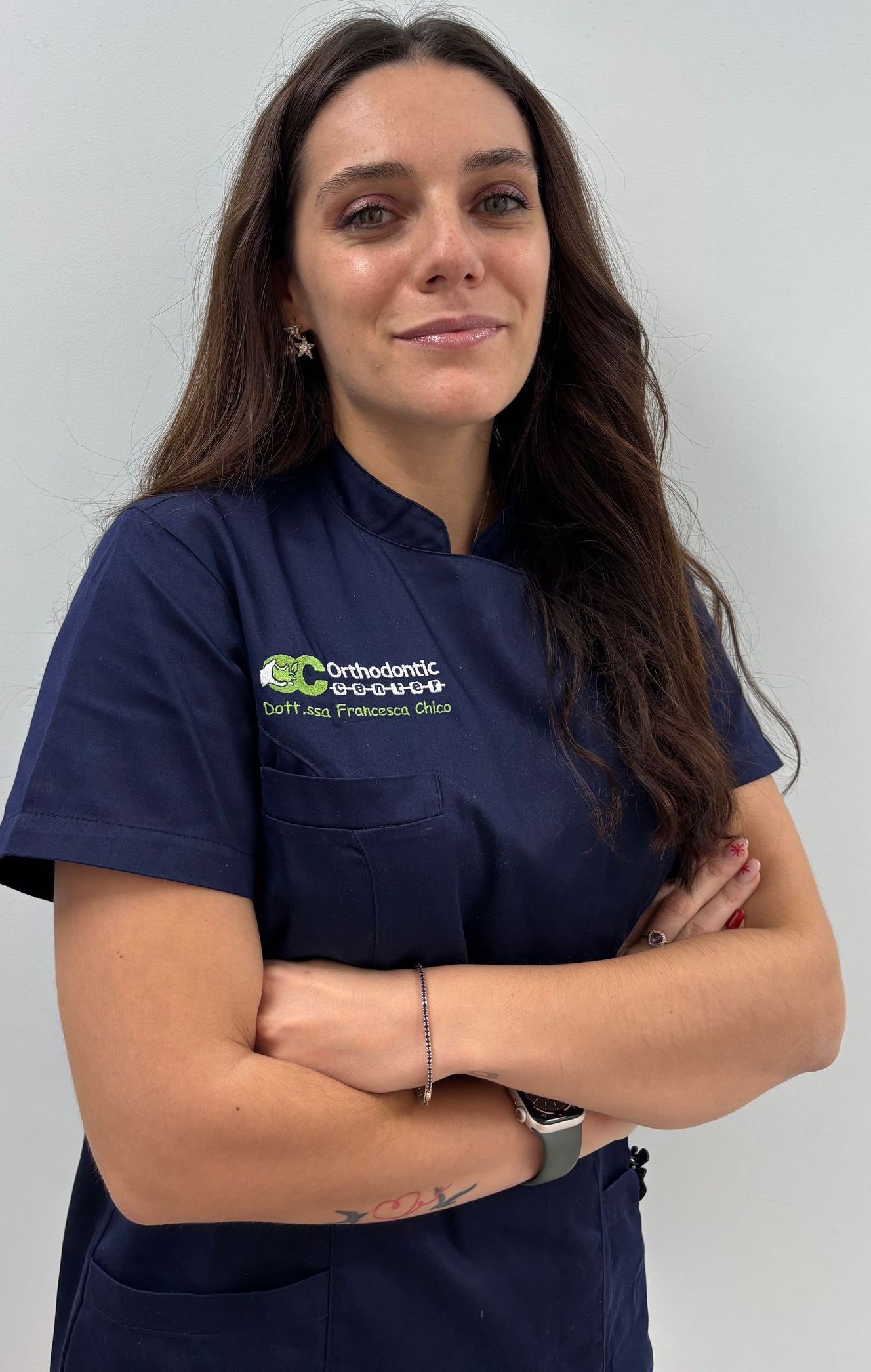 Una donna con una camice blu è in piedi con le braccia incrociate.