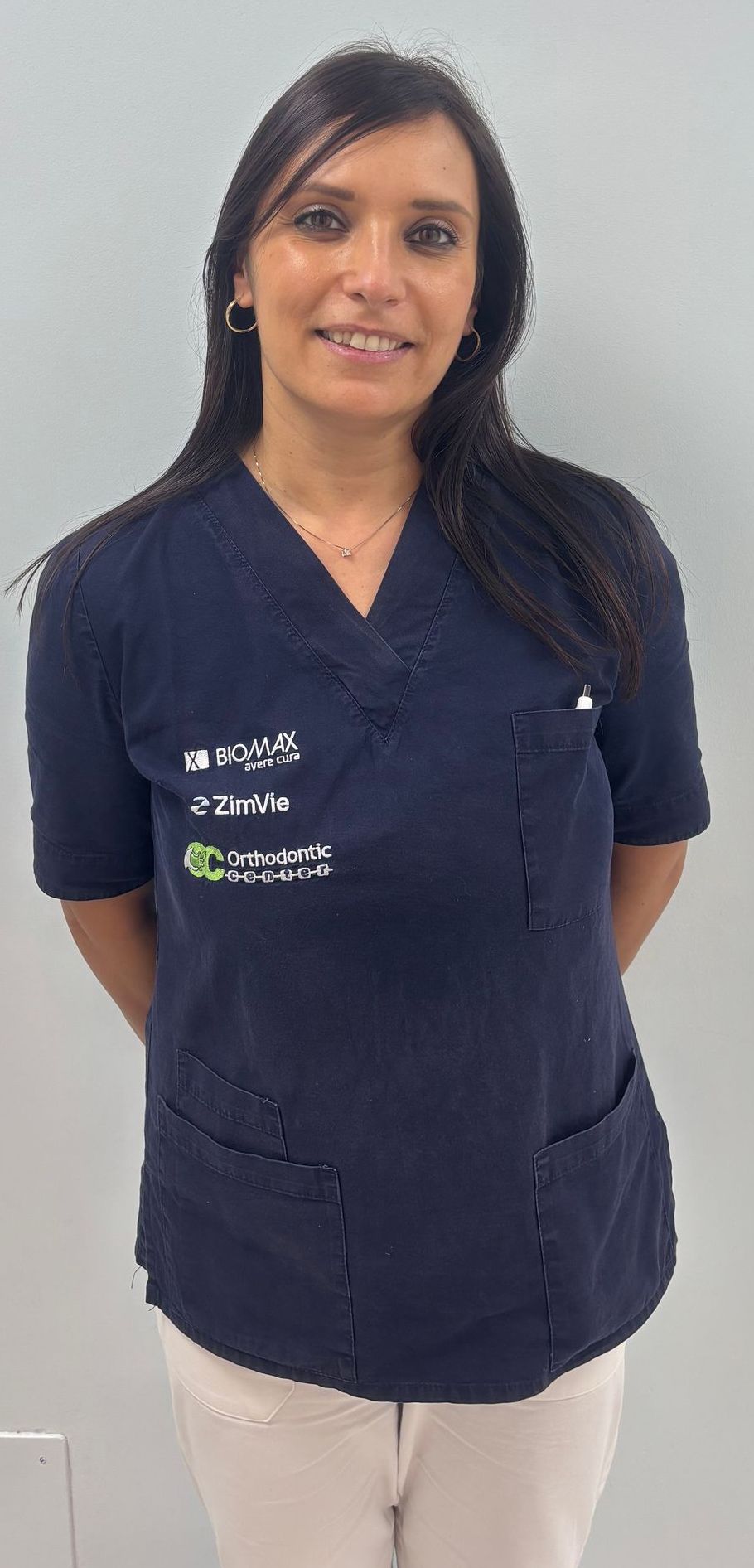 Una donna che indossa una camicetta blu e pantaloni bianchi sorride.