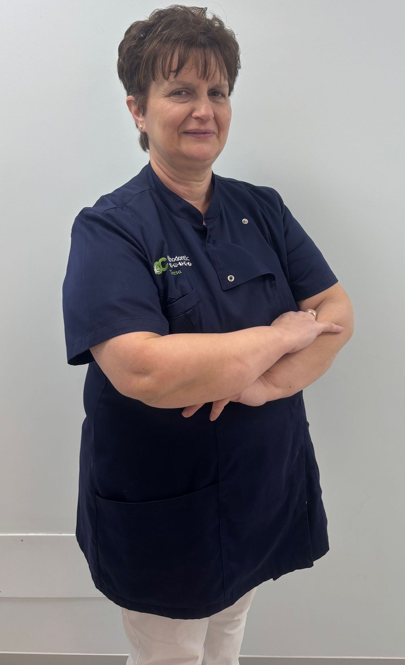 Una donna con una camice blu è in piedi con le braccia incrociate.