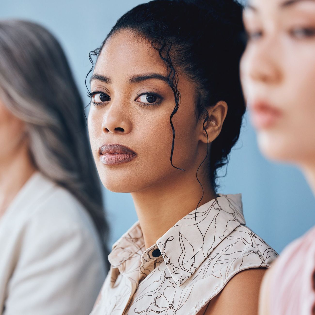 Three women seated in a meeting, with one woman in focus looking at the camera.