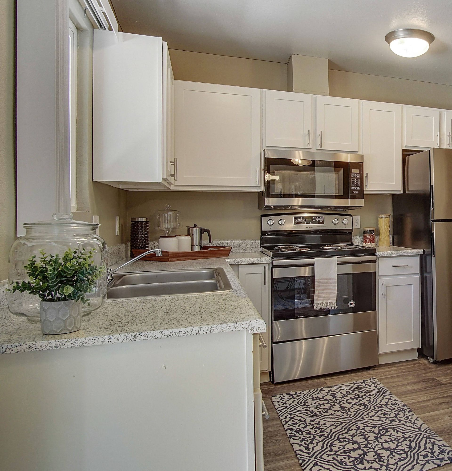 Modern white kitchen with stainless steel appliances and speckled countertops.