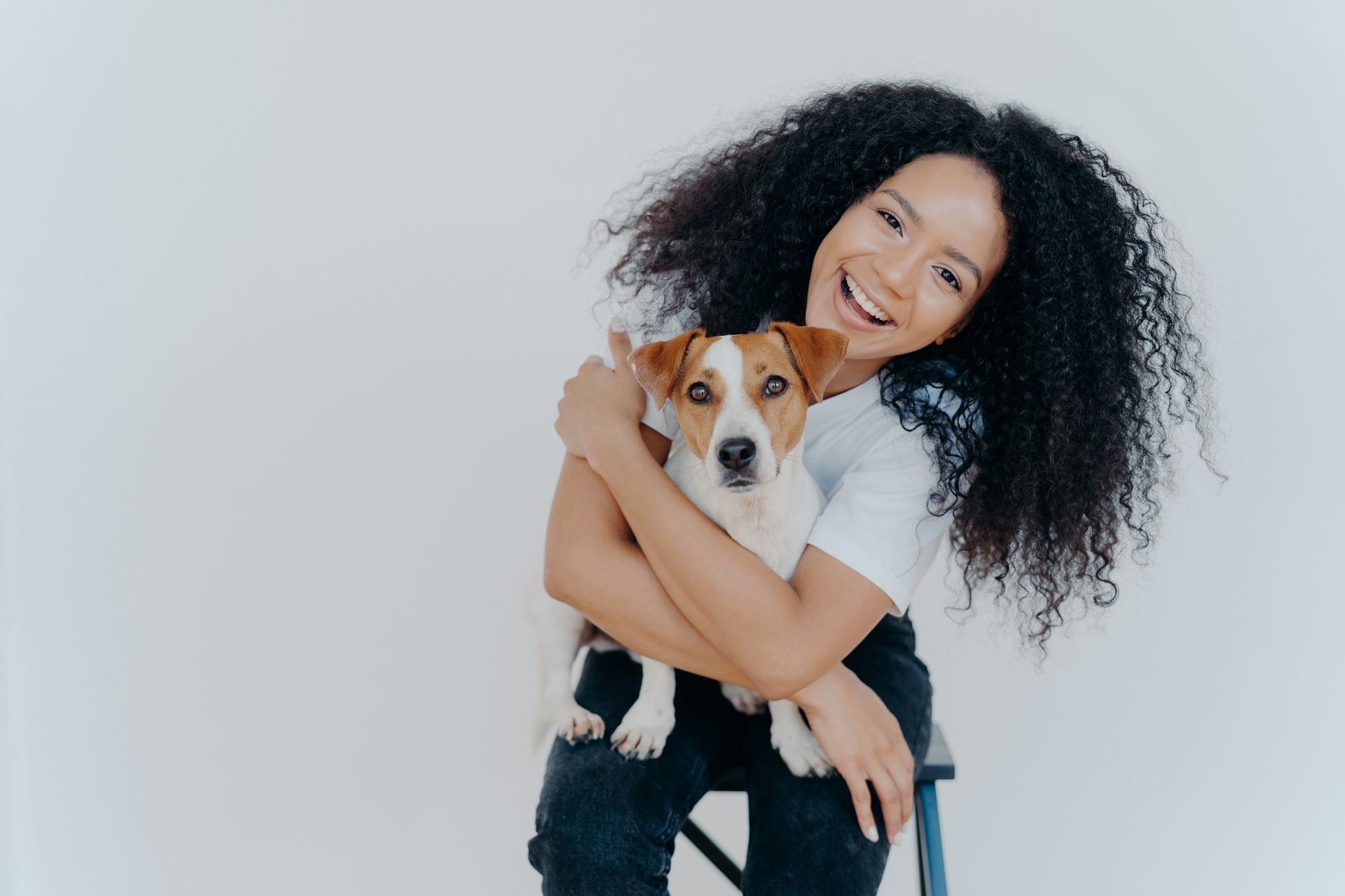 Woman with curly hair smiles while holding a Jack Russell terrier dog against a white background.