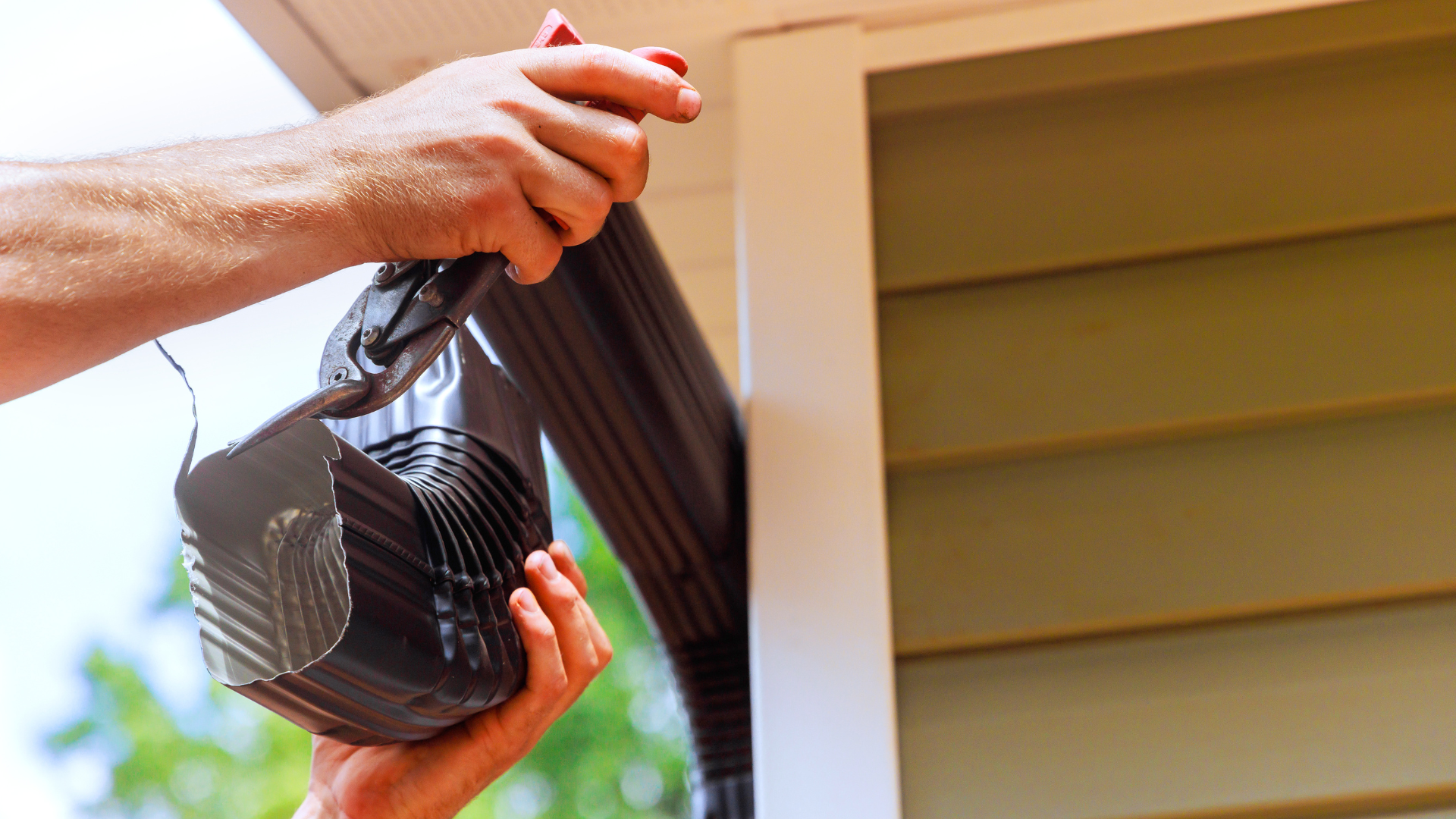 Person in blue uniform fixing a downspout on a house.