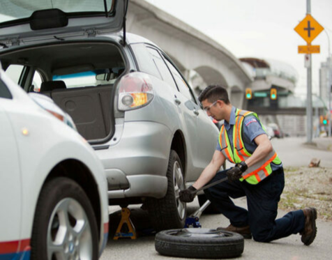 Picture of a road side assistance worker replacing a flat tire on the side of the highway