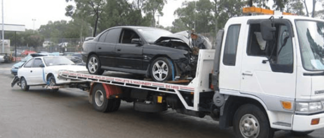 Picture of Flat bed tow truck towing two cars with damage one black one white